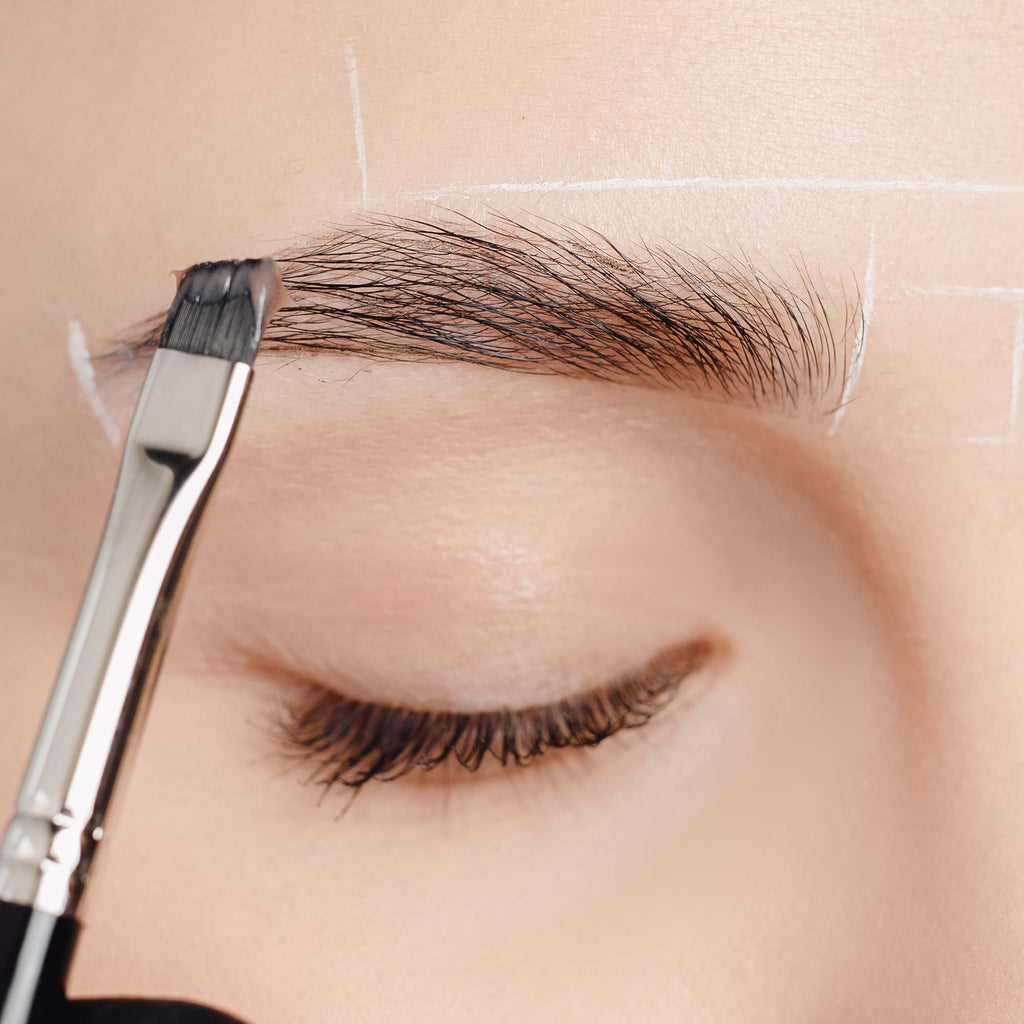 Women with closed eye getting a product brushed onto her eyebrow with a black brush