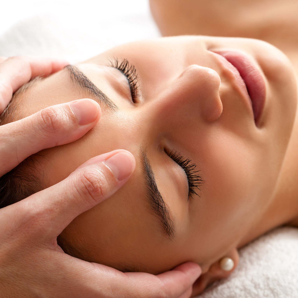 Woman with her eyes closed and a pearl earring getting her head massaged. 