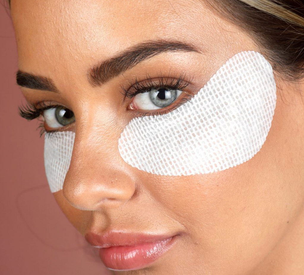 Woman with an o cosmedics no baggage native collagen eye mask under each eye in front of pink background