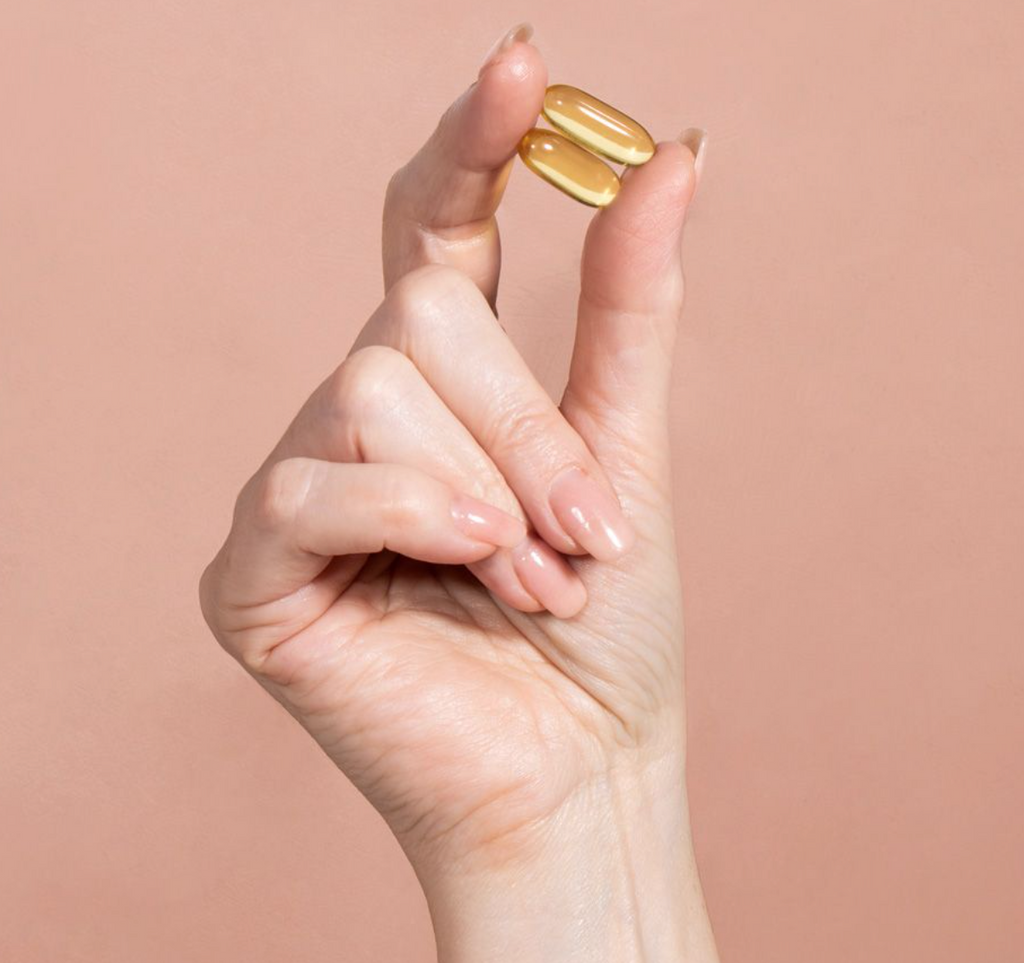 hand holding two yellow capsules between thumb and index finger in front of a pinkish background