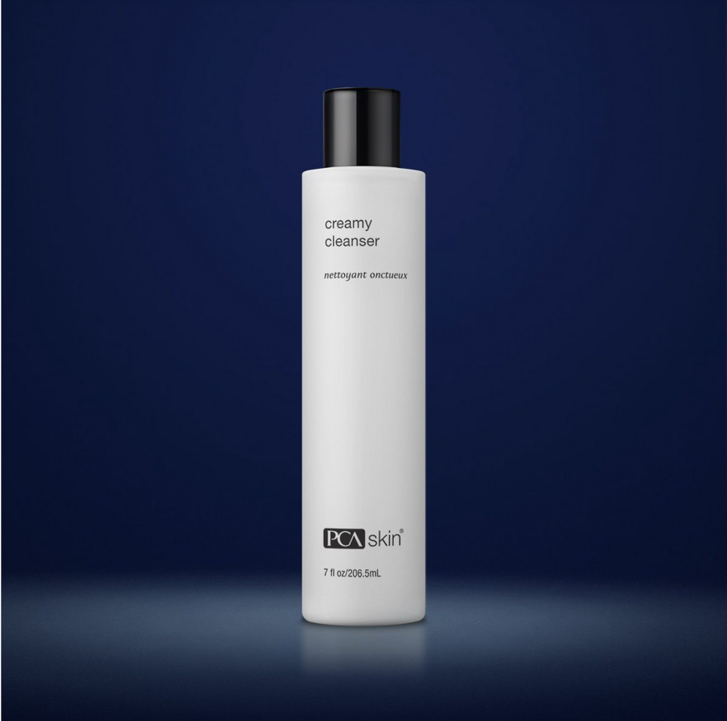PCA Skin creamy cleanser in white container with black lid in front of dark blue background