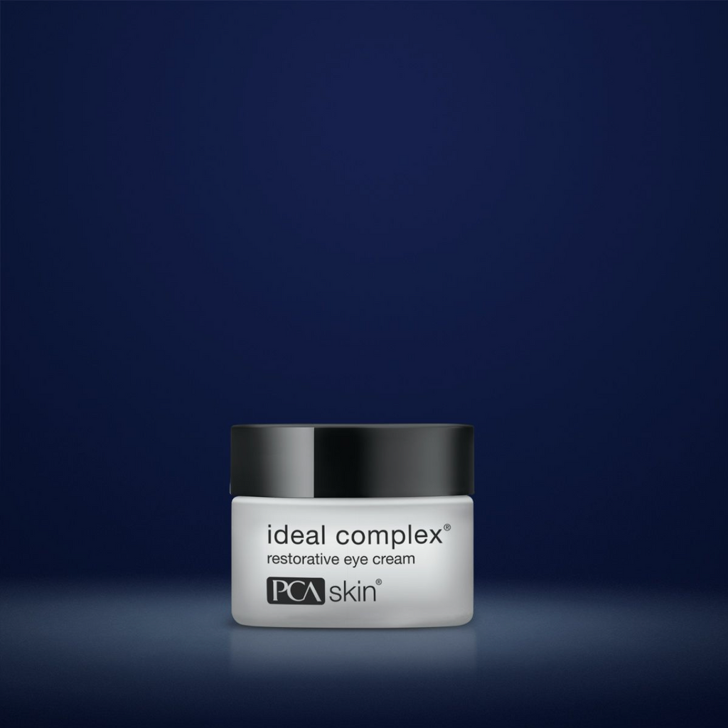 PCA Skin Ideal Complex restorative eye cream in white container with black lid in front of dark blue background