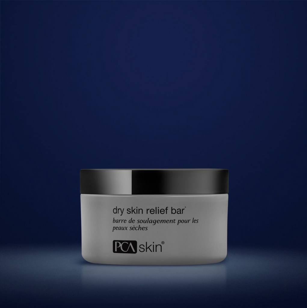 PCA Skin dry skin relief bar in grey container with black lid in front of dark blue background