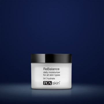 PCA Skin rebalance moisturiser in white container with black lid in front of dark blue background
